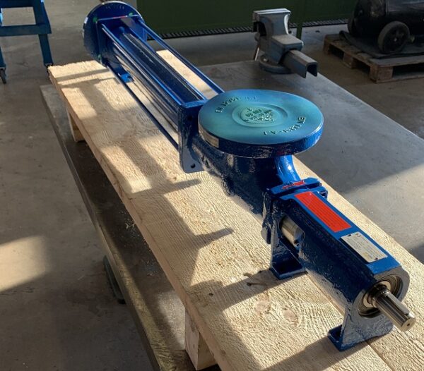 A blue Fludyn BE2H 1500 mono pump / progressive cavity pump without motor. The openings are sealed with caps. The pump is mounted on a narrow wooden pallet for shipping.