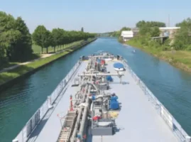 Ein mittelgroßes Tankschiff auf einem Kanal. Man schaut aus dem Führerhaus nach vorne über das Schiff.